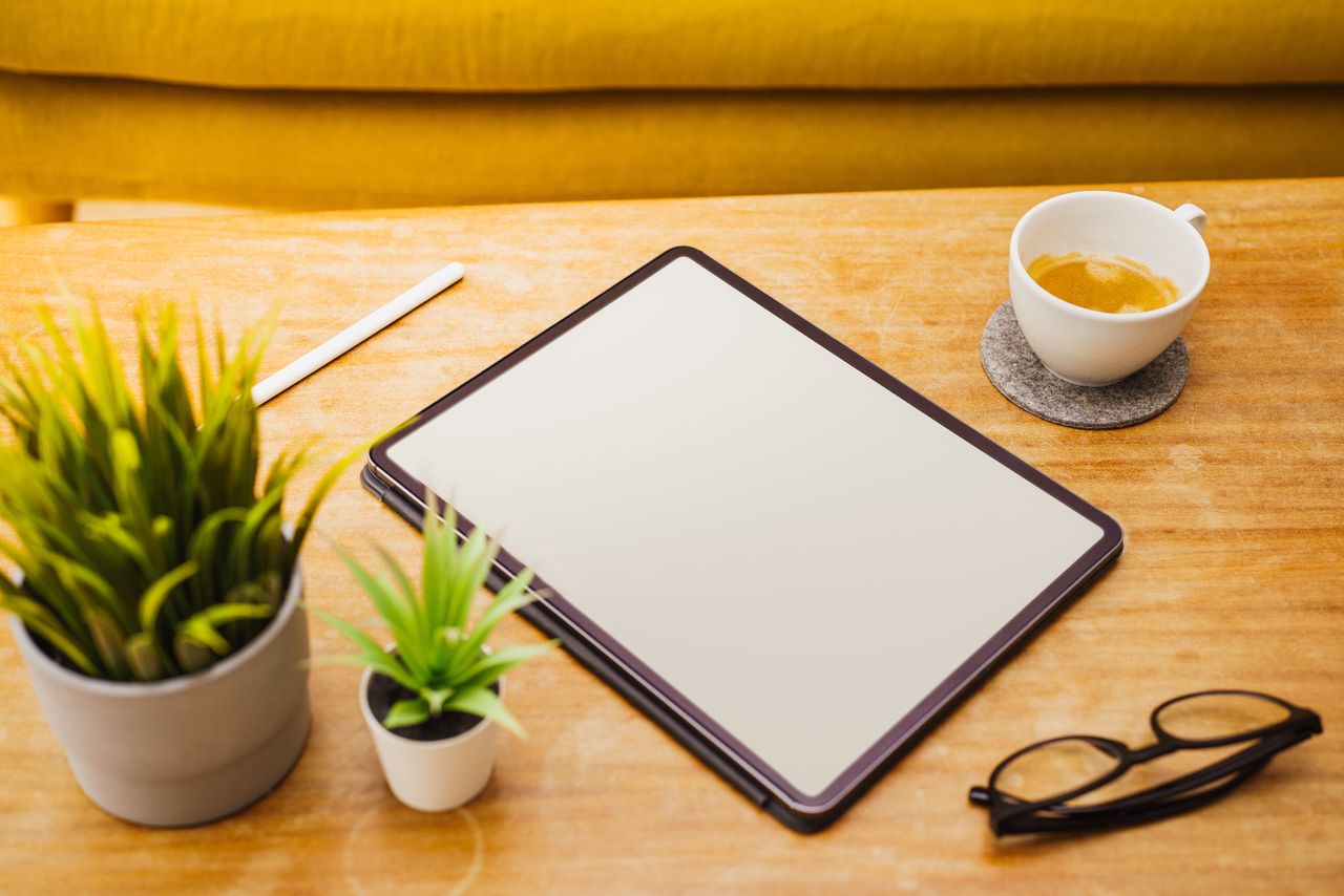 Mastering the First Impression: Your intriguing post title goes here A clean workspace featuring a digital tablet, coffee cup, plants, and eyeglasses on a wooden table.